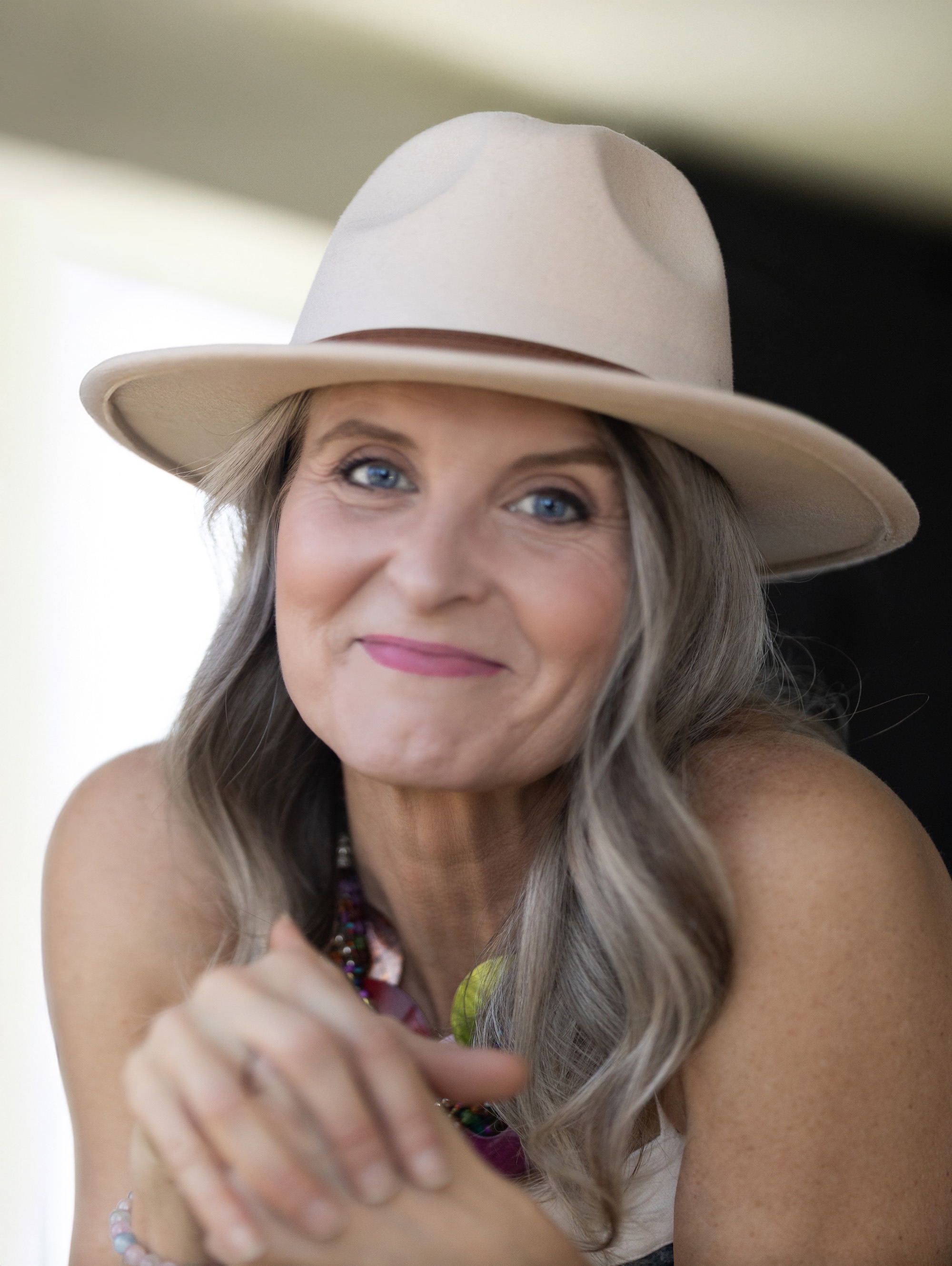Jess Miller, seated and smiling in a cream hat